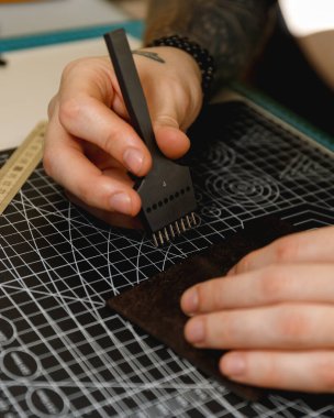 Hand tool punching leather on black cutting mat. The black punch tool rests on a precision cutting mat.