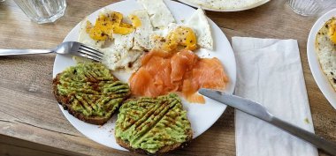 Sağlıklı kahvaltı. Avokado ve tost, somon ve yumurta, tost ve kahve ahşap bir masada.