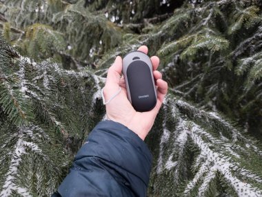 Siyah ceketli bir adam elinde beyaz perdeli bir akıllı telefon tutuyor..