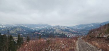 Ağaçlar ve dağlarla çevrili karlı bir yolun yüksek açılı görüntüsü.