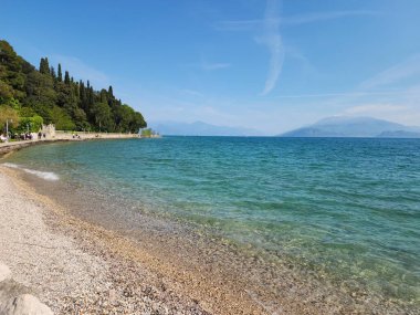 Bu el değmemiş göl manzarası ile sükuneti keşfedin, açık mavi gökyüzü altında yeşil ormanlar tarafından çerçevelenmiş seyahat, doğa ve dinginlik temaları için