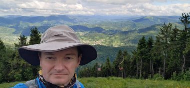 Yeşil gömlekli, sırt çantalı bir turist dağın tepesinde oturur ve mesafeye bakar. Yukarıdan görünüm