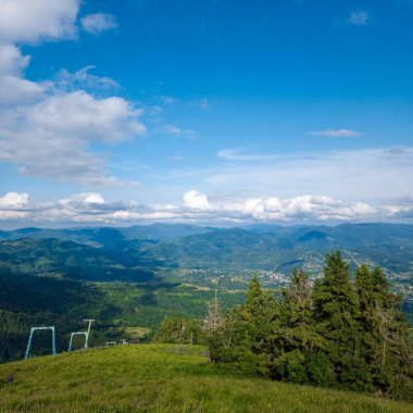 Mavi gökyüzü ve bulutların arkaplanındaki dağlar ve yeşil ağaçların manzarası
