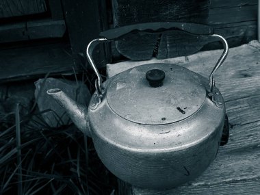 Bahçedeki ahşap masanın saplı eski paslı metal çaydanlık.