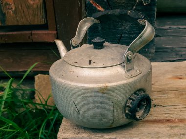 Eski, paslı çaydanlık yeşil çimlerin arkasındaki ahşap masada.