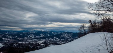 Kış manzarası karla kaplı ağaçlar, bulutlu havada dağlar.