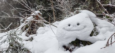 Büyük gri bir kardan adam kışın karların arasında yatıyor.