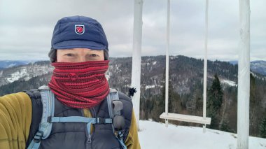 Bir dağın tepesinde sırt çantası olan kışlık ceketli bir turist kız. Kız dağın tepesinde dikiliyordu. Yürüyüş