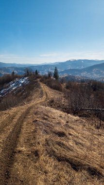 Ağaçlı dağ manzarası ve bulutlu mavi gökyüzü.