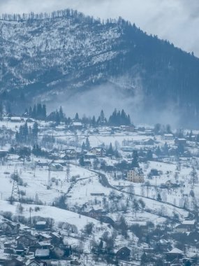 Karla kaplı tepeleri olan köyün kış manzarası