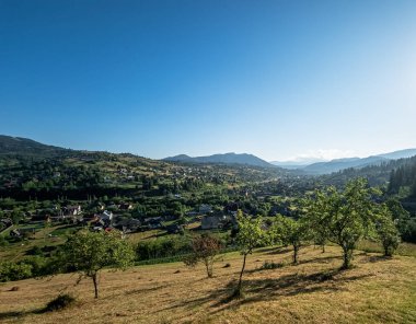 Güneşli yaz gününde dağların ortasında küçük yeşil bir çayırı olan küçük bir köyün güzel manzarası.