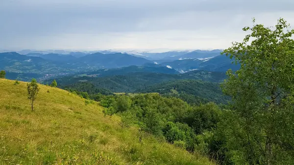 Yeşil dağlar ve arkasında bulutlar olan mavi gökyüzü.