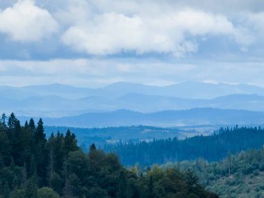 Dağları, ormanı ve bulutları olan güzel bir manzara.