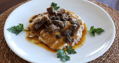 Beyaz bir tabakta sosta servis edilen tavuk ve şampiyon mantarları. İtalyan mutfağı