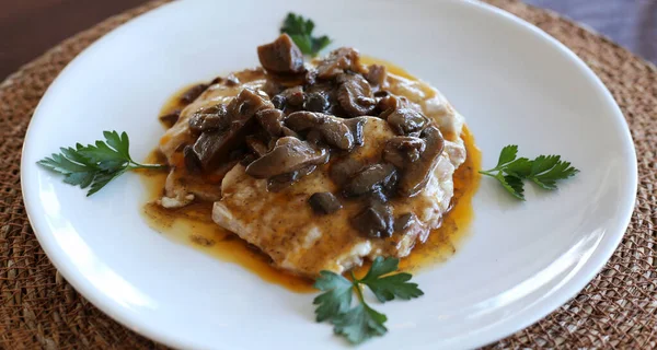 Beyaz bir tabakta sosta servis edilen tavuk ve şampiyon mantarları. İtalyan mutfağı