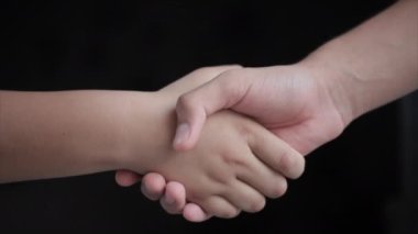 Close-up shot of two people shaking hands, in dark background 4K footage.