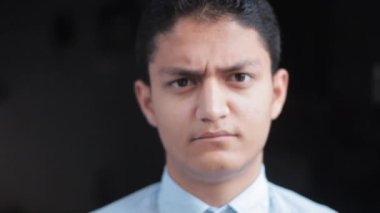 close-up shot of a confused man in a blue shirt making silly, moving eyebrows, and funny faces in black background. 4K footage.