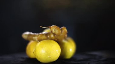 Cinematic close-up shot of fresh lemons, on a black colored shiny wooden surface. Fresh green vegetables in wicker basket.4K - 24fps