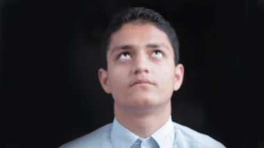 A young teen boy showed his face wearing a blue colored shirt with a dark black background.