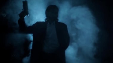 Shot of a young assassin with long hair. A young hitman with long hair coming from the darkness and shooting bullets, Cinematic light, and some smoke. HD footage 24 FPS.