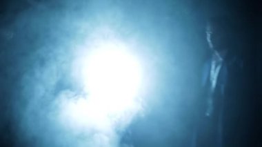 Shot of a young assassin with long hair. A young hitman with long hair coming from the darkness and shooting bullets, Cinematic light, and some smoke. HD footage 24 FPS.