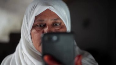 Beyaz tesettürlü Müslüman bir kadın siyah telefon kullanıyor ve gülümsüyor. Müslüman kadın teknolojiyi kullanıyor.