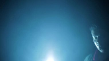 Cinematic shot of a man in a long coat with some blood on his face standing in front of the light, with added smoke. HD footage 24FPS.