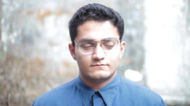 Portrait shot of a young male with glasses looking tired and trying to look energetic. Tired student.
