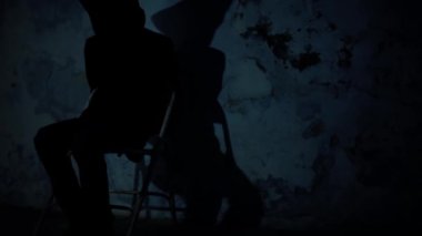 Sandalyede oturan bir adamın sinematik görüntüsü. Yüzü siyah bir bezle örtülmüş ve elleri bağlı. Karanlık dramatik ışık. Hd görüntüleri.