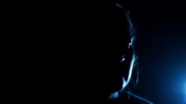 Bir kadının yüzünün yarısında ışıkla bir sandalyede oturmasının sinematik çekimi, dramatik bir ışık. HD görüntüler.