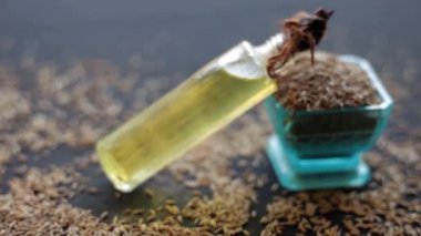 Siyah ahşap bir yüzey üzerinde ham kimyon tohumları (Cuminum cyminum) ile birlikte şeffaf bir şişedeki jeera yağının HD görüntüsü.