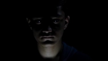 Korkmuş bir çocuğun karamsar dramatik bir ışıkla vuruluşunun sinematik çekimi. Korkmuş yüz ifadeleri. 24FPS 'te HD görüntüler.