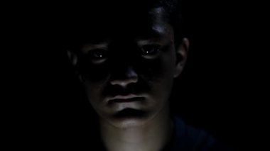 Korkmuş bir çocuğun karamsar dramatik bir ışıkla vuruluşunun sinematik çekimi. Korkmuş yüz ifadeleri. 24FPS 'te HD görüntüler.