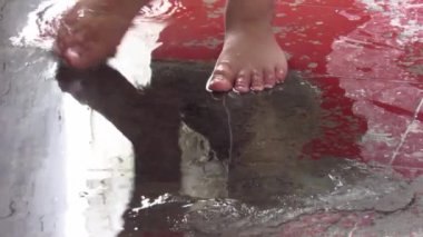 Kırmızı zeminde toplanan yağmur suyuyla oynayan insan ayaklarının yakın plan çekimi, HD görüntüler. Su birikintileriyle eğlen..