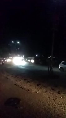 Yağmurlu bir gecede sokak lambaları altında parıldayan ıslak yansımaları olan bozuk asfalt bir yolda araba, bisiklet ve diğer araçların trafiğini hareket ettirmek, yüksek çözünürlüklü sinematik tarzda kentsel yaşamı gözler önüne sermek.