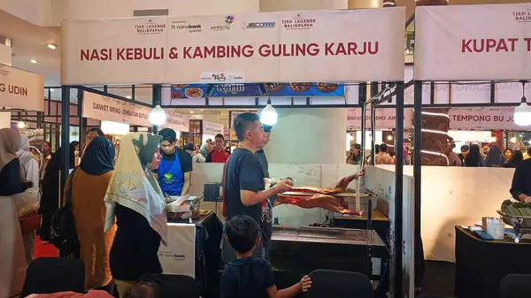 Balikpapan, Endonezya - 19 Temmuz 2024: İnsanlar, Endonezya 'daki canlı bir yemek festivalinde ızgara kuzu ve Nasi Kebuli ikram eden bir gıda tezgahının etrafında toplanıyorlar. Endonezya 'nın efsanevi yemek festivalinde atmosfer canlı ve hareketli..