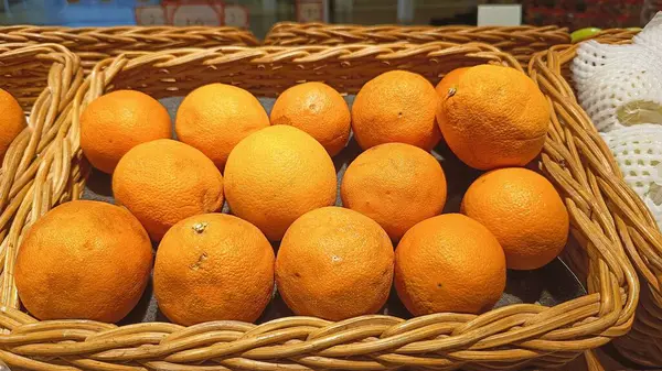 Bir süpermarkette hasır sepetlere yerleştirilmiş taze portakalların yakın plan görüntüsü canlı renkler ve sağlıklı ürünler sergiliyor. Portakallar tatlı meyveleri için tropikal alanlarda yaygın olarak yetişir ve iyi bir lif ve potasyum kaynağıdır..