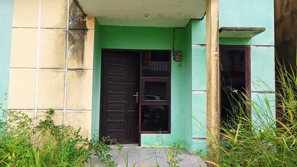 Yeşil bir evin dış tarafında geleneksel ahşap bir kapı. Çevreleyen bitkiler, somut kırsal cazibe ve canlı renkler. Mimarlık, tasarım ve ev girişi konuları için ideal. Ev kiralamak ya da ev satmak için uygun..