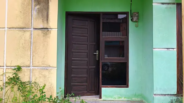 Ahşap kapılı yeşil bir binanın dış görünüşü, aşırı büyümüş çimenler ve yıpranmış dokular, ihmal ve kentsel bozulmayı akla getiriyor. Kabataslak bir cazibe, bina veya ev teması için mükemmel..