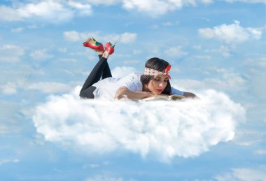 Güzel genç kız bulutların üzerinde uzanıyor ve kitap okumaktan zevk alıyor. Kapat.