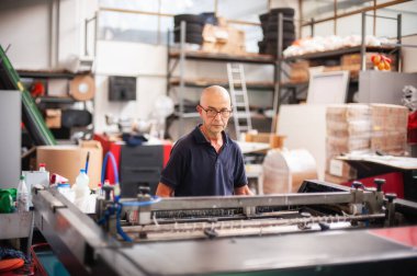 Matbaada, deneyimli bir teknisyen ekran baskı makinesi üzerinde çalışıyor. Üretim işi. Yazdırma kalitesini kontrol et.