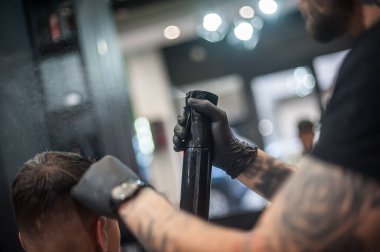 Modern şehir kuaförü saç spreyiyle saç stilini düzeltiyor ve havada damlalar görünüyor.