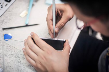 İş yeri üst görünümü, yakın plan. Bir elektronik tamir atölyesinde, tamirci akıllı telefonu tamir eder, cımbızı bir çok iş aletinden biri olarak kullanır.