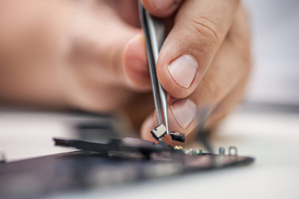 Workplace top view, close-up. In an electronics repair shop, a repairman repairs a smartphone, uses tweezers as one of the many work tools.