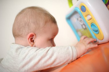 Baby plays with toys. Close-up view of cute baby boy lies on its stomach with an outstretched hand holding a toy and learns about the world around him