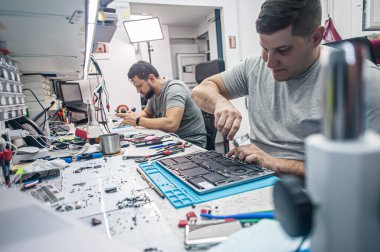 Technical support and fixing gadgets problems. Servicing, repairing, cleaning, maintaining computers. Repair shop. Hardware maintenance. Male technicians fixing disassembled laptop parts. 