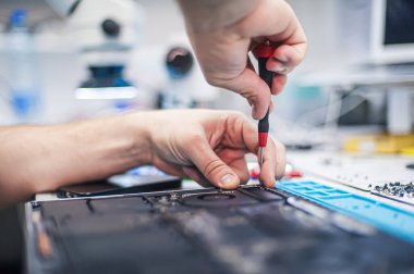 Technical support and fixing gadgets problems. Servicing, repairing, cleaning, maintaining computers. Repair shop. Hardware maintenance. Male technicians fixing disassembled laptop parts. 