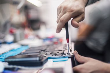 Technical support and fixing gadgets problems. Servicing, repairing, cleaning, maintaining computers. Repair shop. Hardware maintenance. Male technicians fixing disassembled laptop parts. 