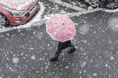 People walks on the urban city street on a snowy winter day with small white snow snowflakes in foreground