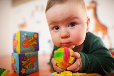 Portrait of cute baby boy playing with colorful toys at home. Close-up view of cute baby boy lies on its stomach and plays with toys. Playground for babies